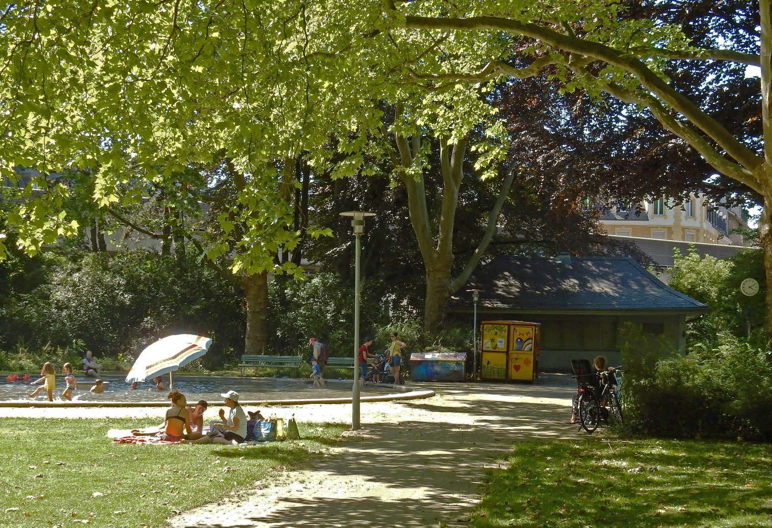 Besuchende im Sihlhölzlipark. Im Hintergrund das Planschbecken und das noch unrenovierte Kioskgebäude im Sommer 2020 (Foto: D. Sauter, 2020).